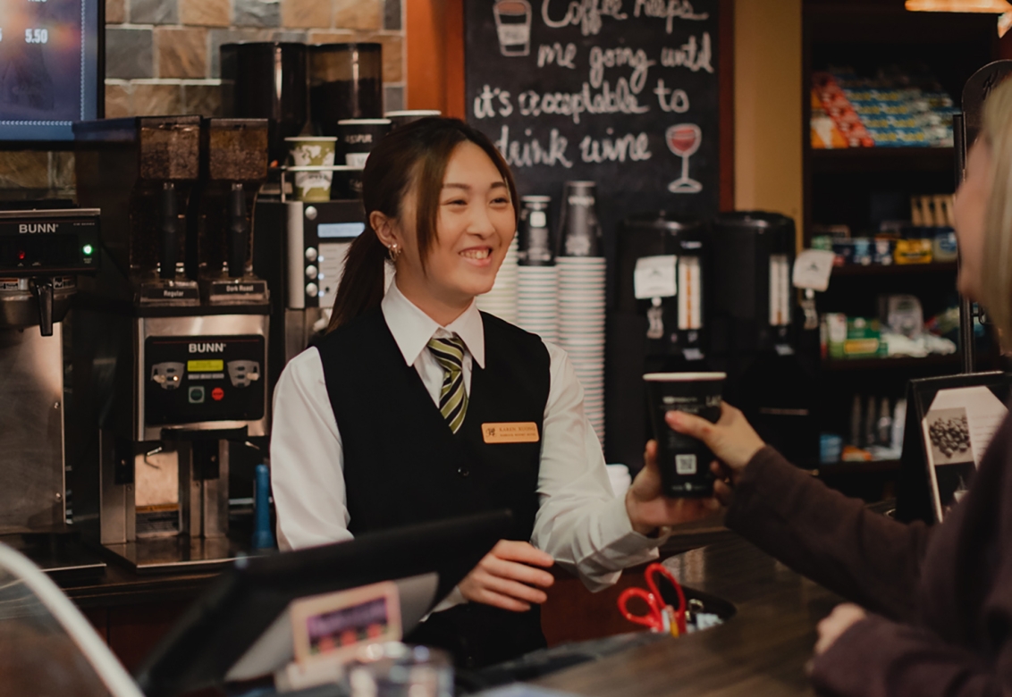 A smiling barista giving a cup to a customer