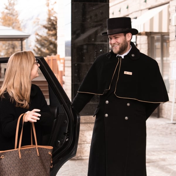 A man in a top hat opening the car door for a woman