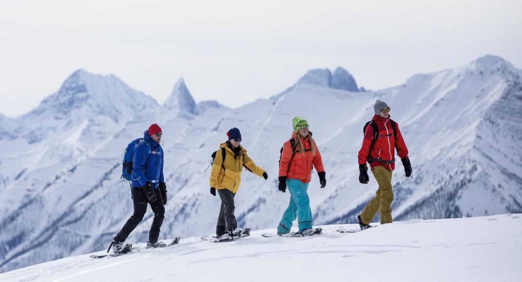 A group of people enjoying a show shoe adventure with snow covered mountains in the background in Banff National Park.