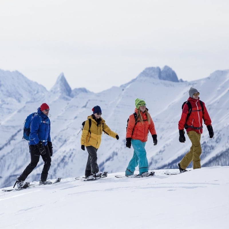 A group of people enjoying a show shoe adventure with snow covered mountains in the background in Banff National Park.