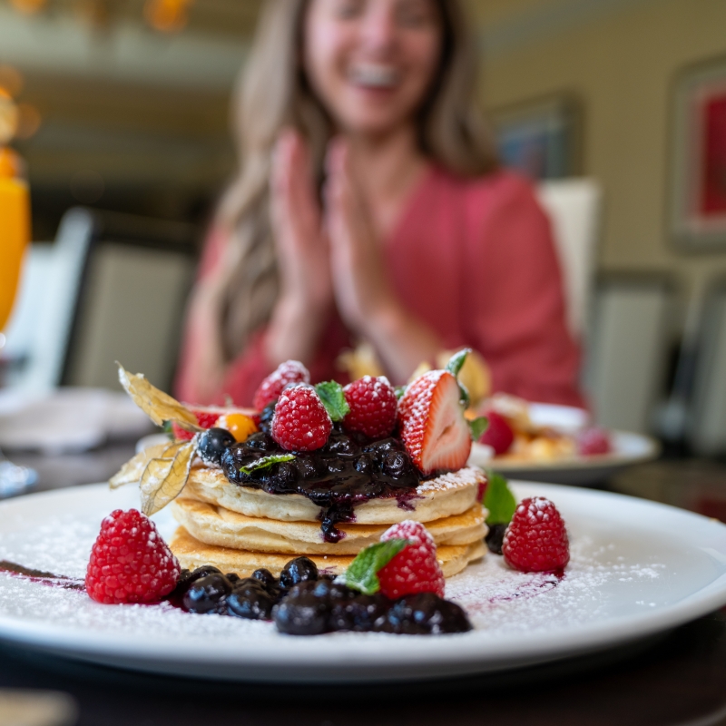 Person in background is gleeful over the mountain of berry pancakes