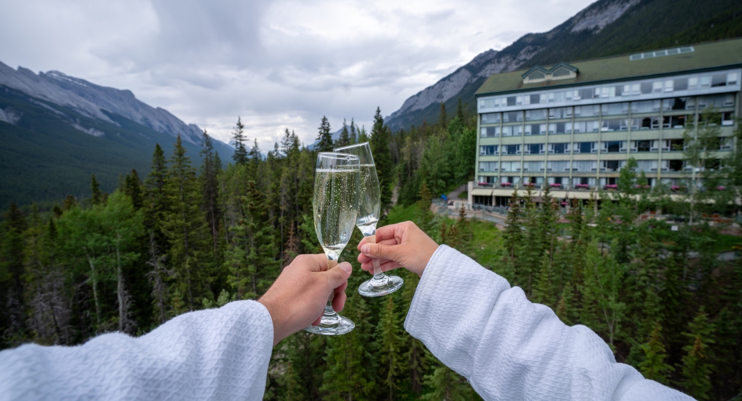 Two glasses of bubbly wine clinking with The Rimrock Resort Hotel and the mountains in the background