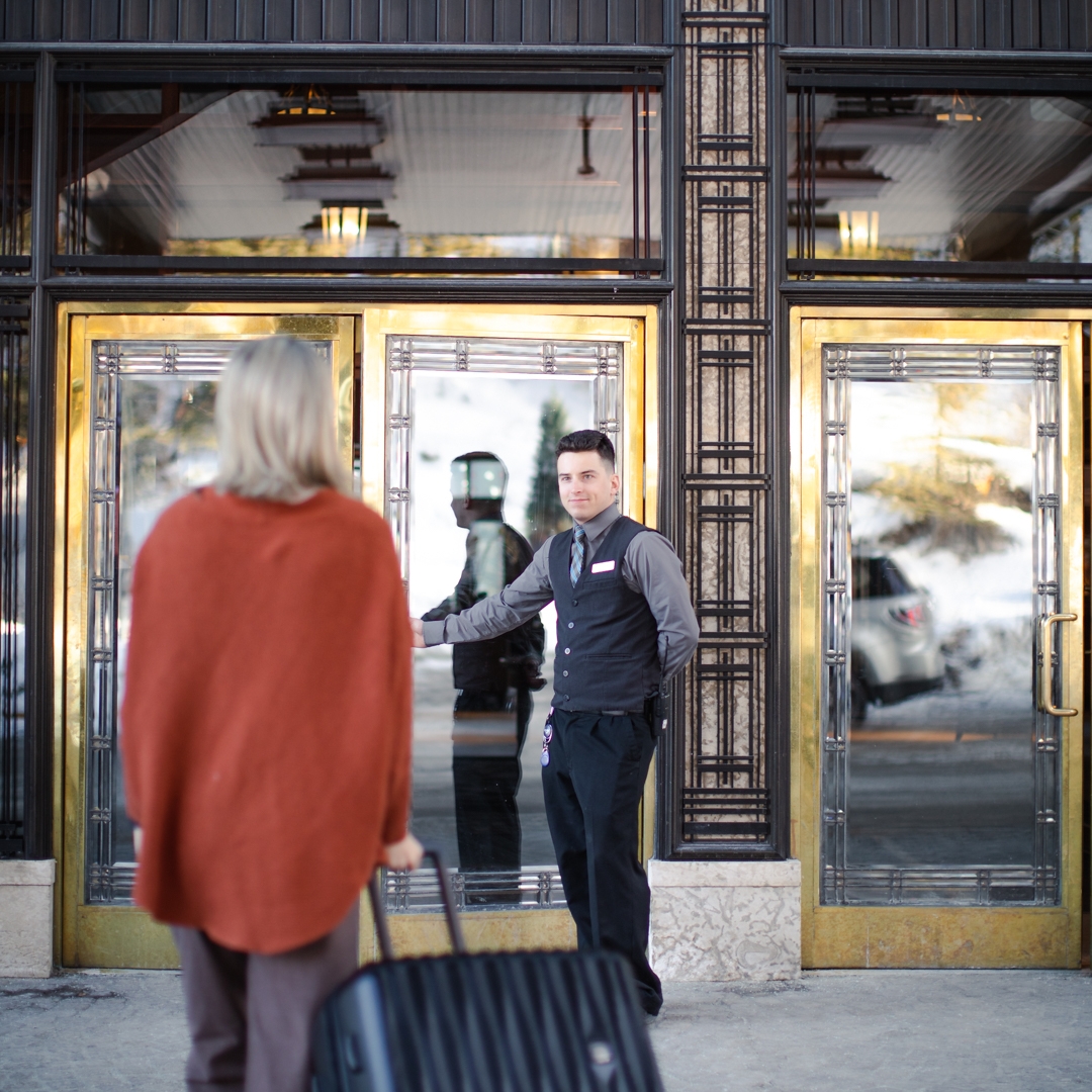 A man opening the door for someone with a suitcase