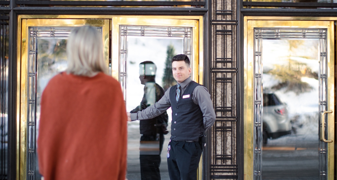 A man opening the door for someone with a suitcase