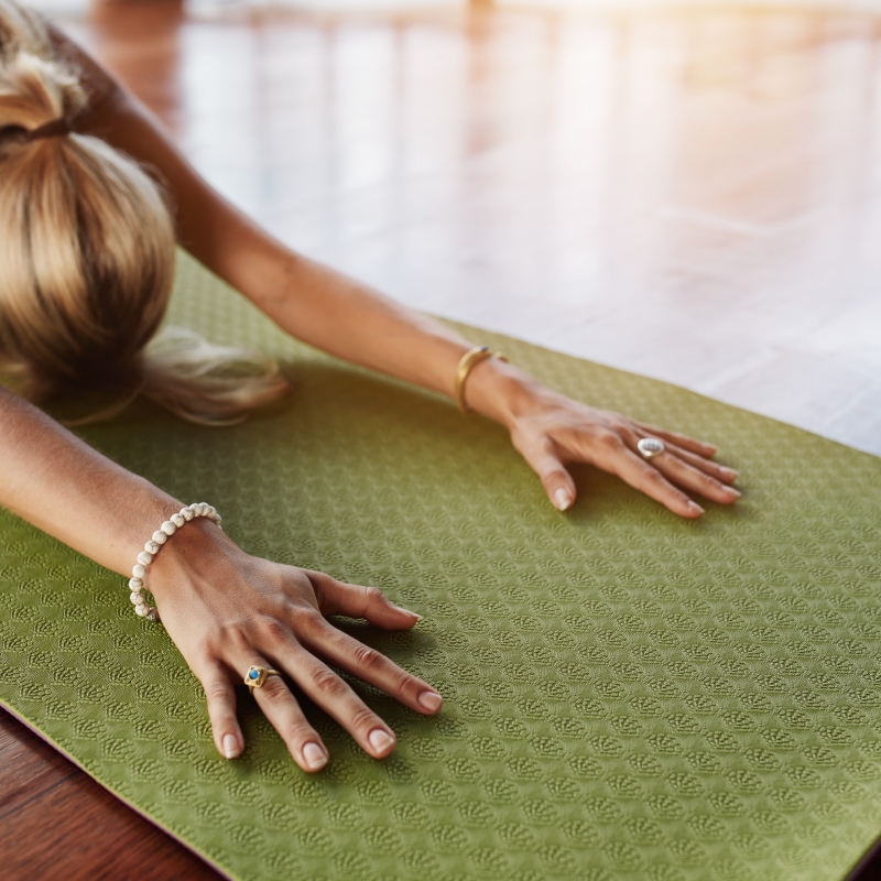 Female doing stretching workout on exercise mat. Woman doing balasana yoga at gym, with focus on hands.