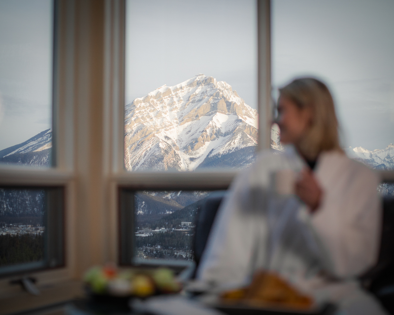Women in robe drinking coffee looking out the window at the mountains in Banff