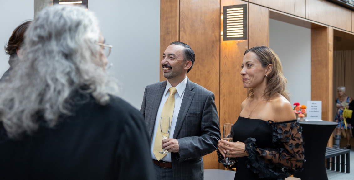 Guests chatting during a reception at The Whyte Museum, holding champagne glasses in a bright space with warm wood paneling and modern wall lighting.