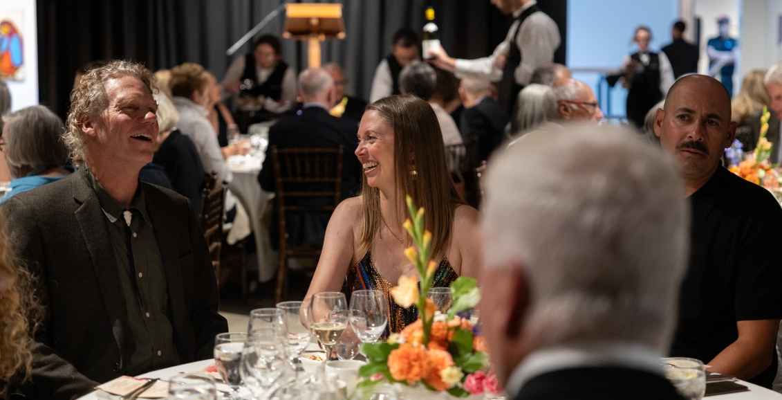 Guests seated at a dinner table at The Whyte Museum, smiling and talking while servers pour wine in the background during an evening event.