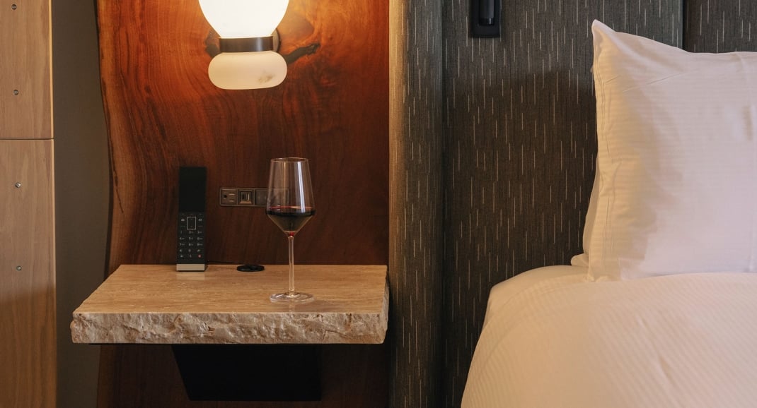 A bed from Rimrock Banff, Emblems Collection with a side stand and glass of red wine.