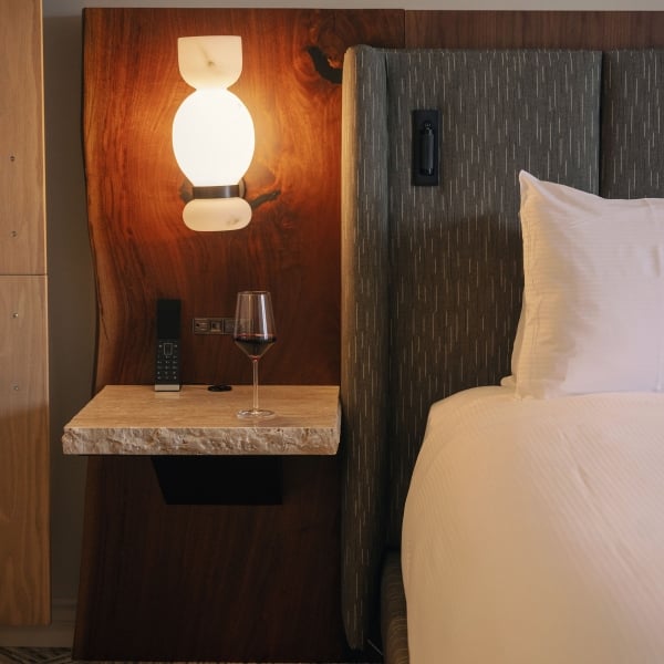 A bed from Rimrock Banff, Emblems Collection with a side stand and glass of red wine.