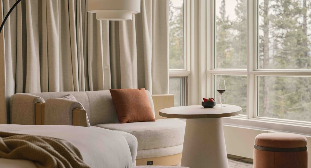 a bed in a Classic room at Rimrock Banff, Emblems Collection with a table in the background and a forest view out the window