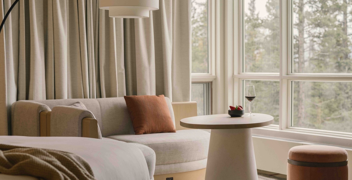 a bed in a Classic room at Rimrock Banff, Emblems Collection with a table in the background and a forest view out the window