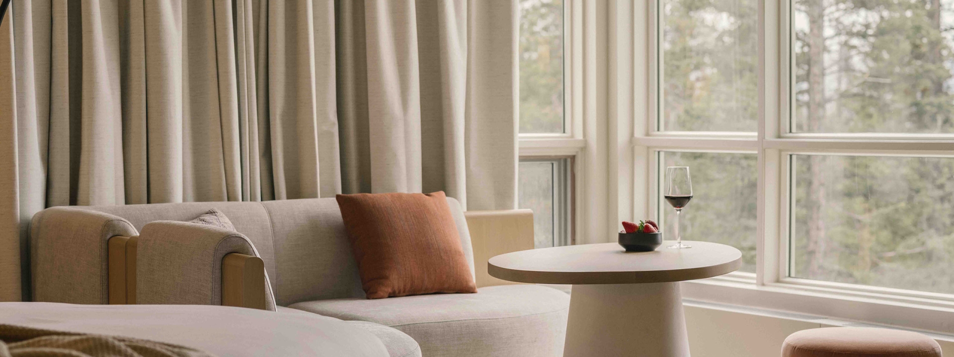 a bed in a Classic room at Rimrock Banff, Emblems Collection with a table in the background and a forest view out the window