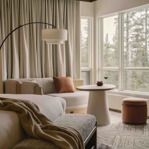 a bed in a Classic room at Rimrock Banff, Emblems Collection with a table in the background and a forest view out the window