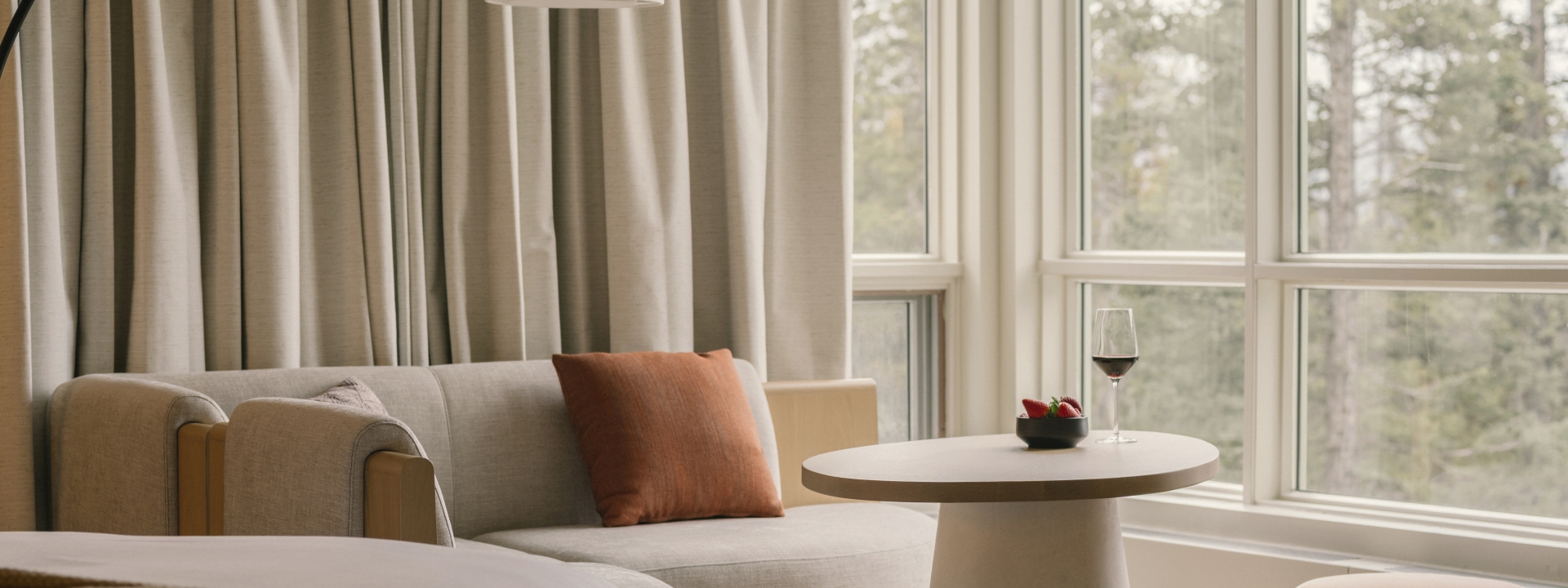 a bed in a Classic room at Rimrock Banff, Emblems Collection with a table in the background and a forest view out the window