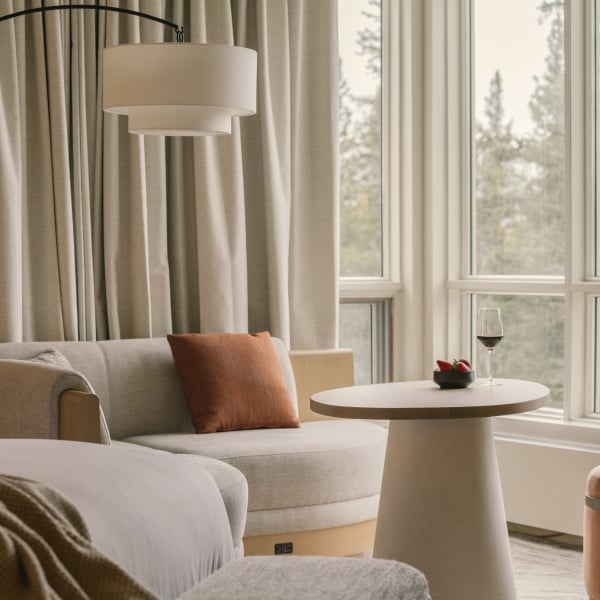 a bed in a Classic room at Rimrock Banff, Emblems Collection with a table in the background and a forest view out the window