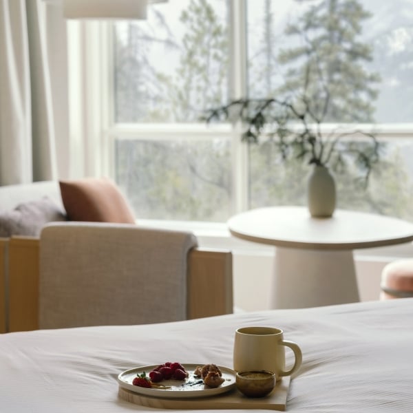 The bed with a coffee and pastry on it in a Classic Room at Rimrock Banff, Emblems Collection