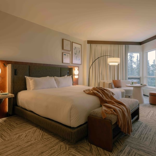 A room at Rimrock Banff, with warm finishes, a cozy bed and a sitting area by the window.