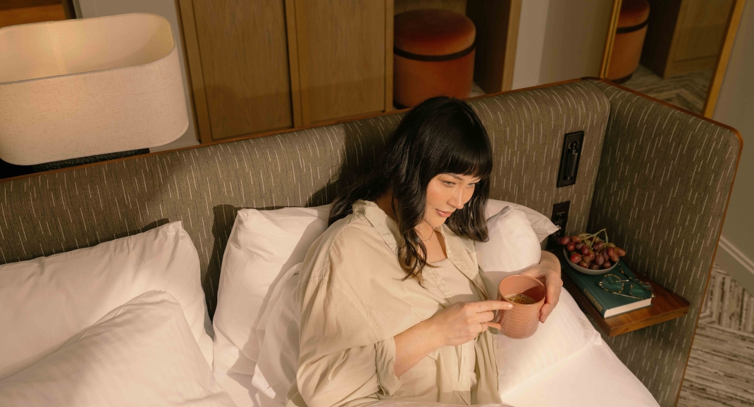 A woman sitting in the bed at Rimrock looking out the window with sun rays on her face.