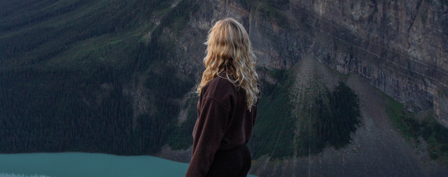 Hiker standing on a cliff edge overlooking Lake Louise and the surrounding mountains from the Little Beehive trail at dawn.