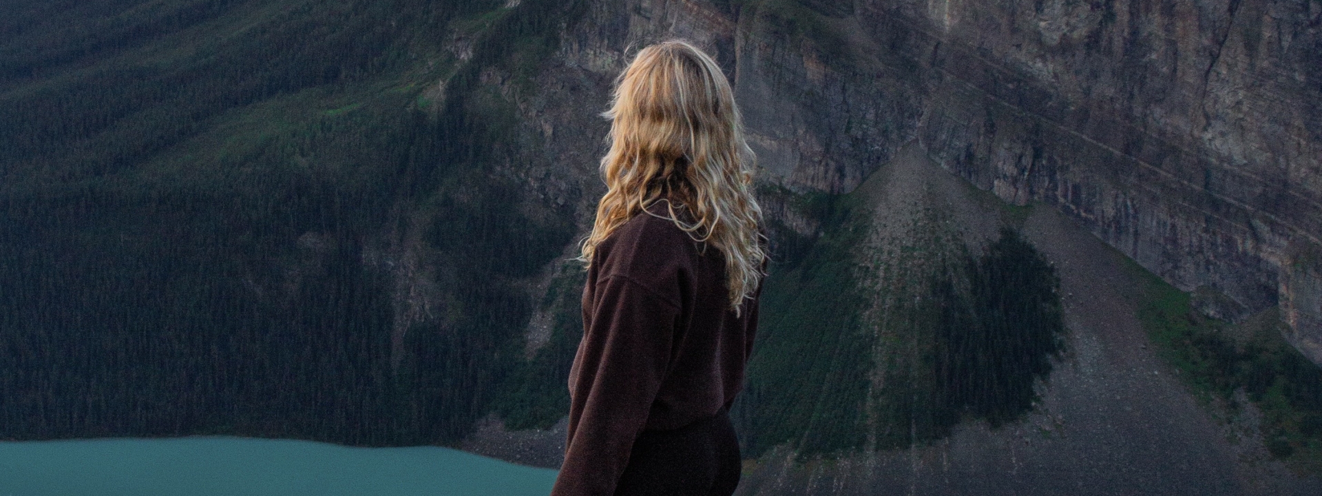 Hiker standing on a cliff edge overlooking Lake Louise and the surrounding mountains from the Little Beehive trail at dawn.