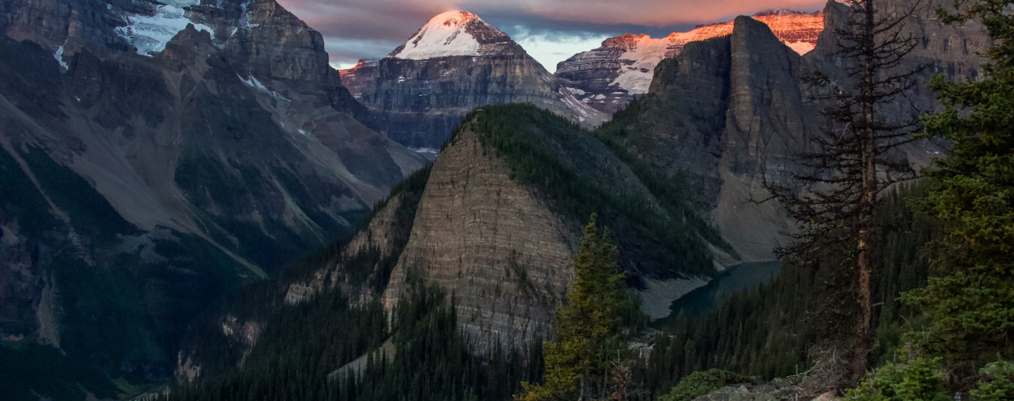 Early morning alpenglow illuminating rugged peaks and forested valleys as seen from the Little Beehive trail near Lake Louise.