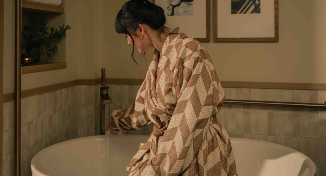 A woman staying at a suite at Rimrock Banff, sitting on the side of her soaker tub in a robe before taking a bath.