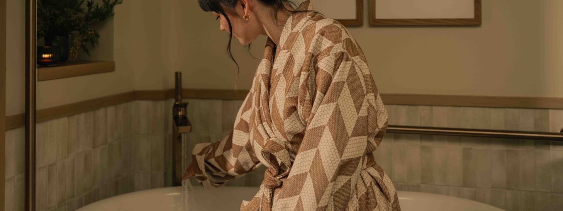 A woman staying at a suite at Rimrock Banff, sitting on the side of her soaker tub in a robe before taking a bath.