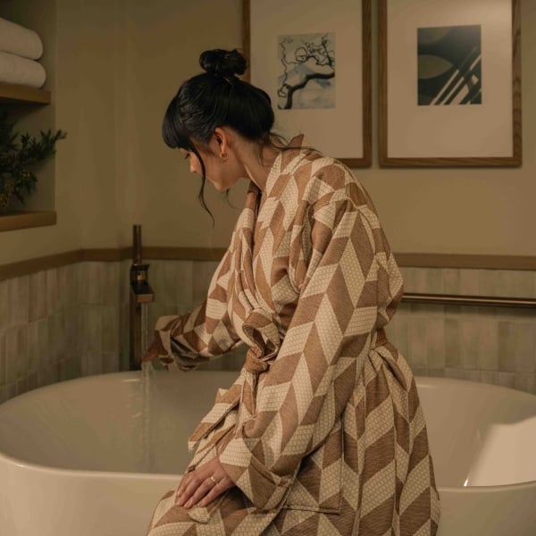 A woman staying at a suite at Rimrock Banff, sitting on the side of her soaker tub in a robe before taking a bath.
